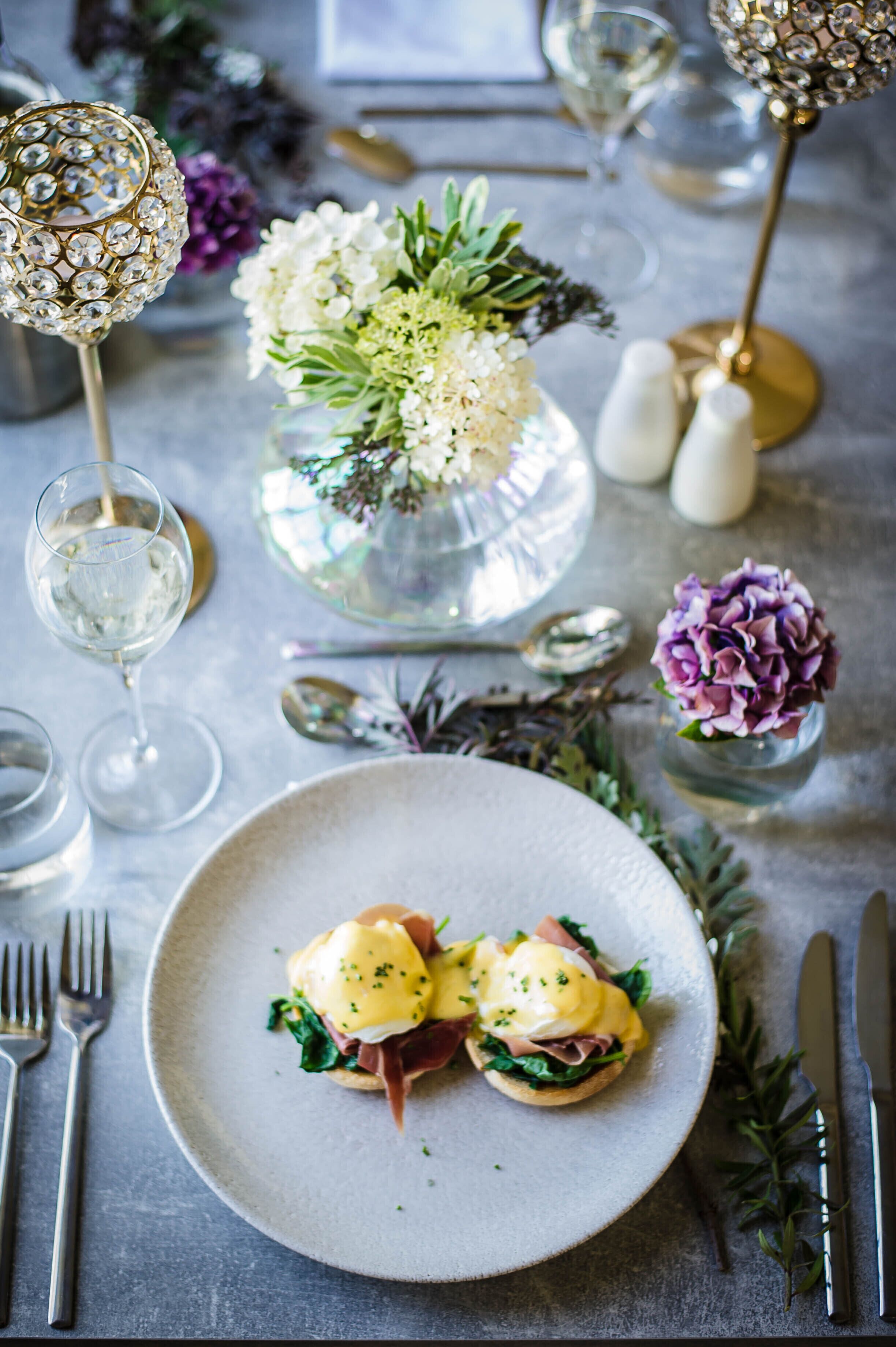 A dining table with a plate of food, a vase with flowers, and a decorative lamp.