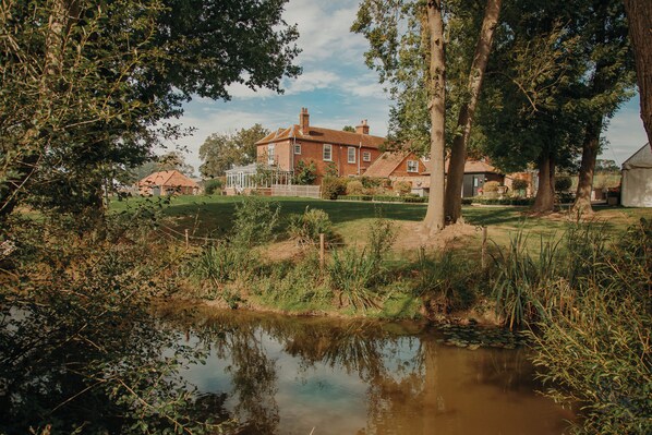 A large brick house with a well-maintained lawn and a small pond in the foreground. - Downham Hall (Billericay)