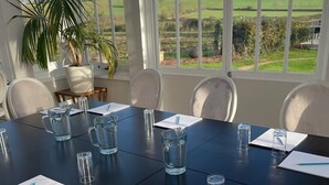 Un salón de conferencias con una gran mesa, sillas y una planta en maceta.