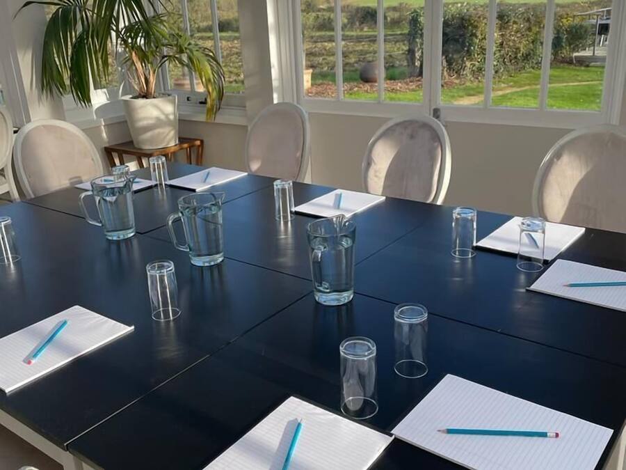 Un salón de conferencias con una gran mesa, sillas y una planta en maceta.