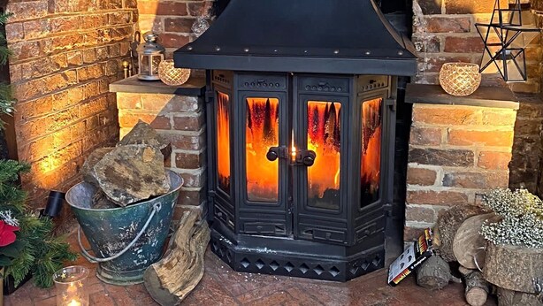 Una chimenea de piedra con una repisa negra, leña y un farol decorativo.