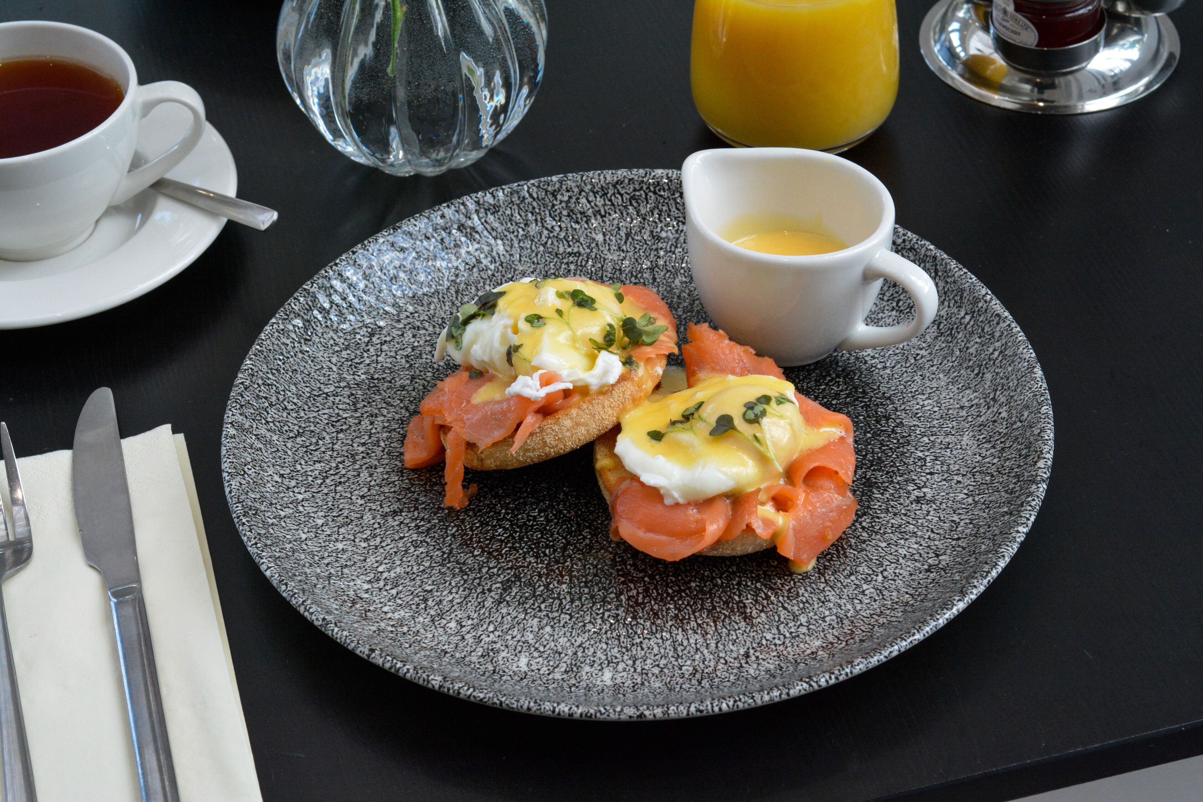 A breakfast plate with eggs, smoked salmon, and toast, accompanied by a cup of tea and a glass of orange juice.