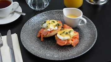 A breakfast plate with eggs, smoked salmon, and toast, accompanied by a cup of tea and a glass of orange juice.
