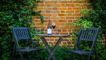 Two black chairs and a table with a bottle and glass of wine against a brick wall.