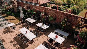 Une terrasse extérieure dotée de plusieurs tables et chaises, entourée de murs en briques et agrémentée de plantes en pot.
