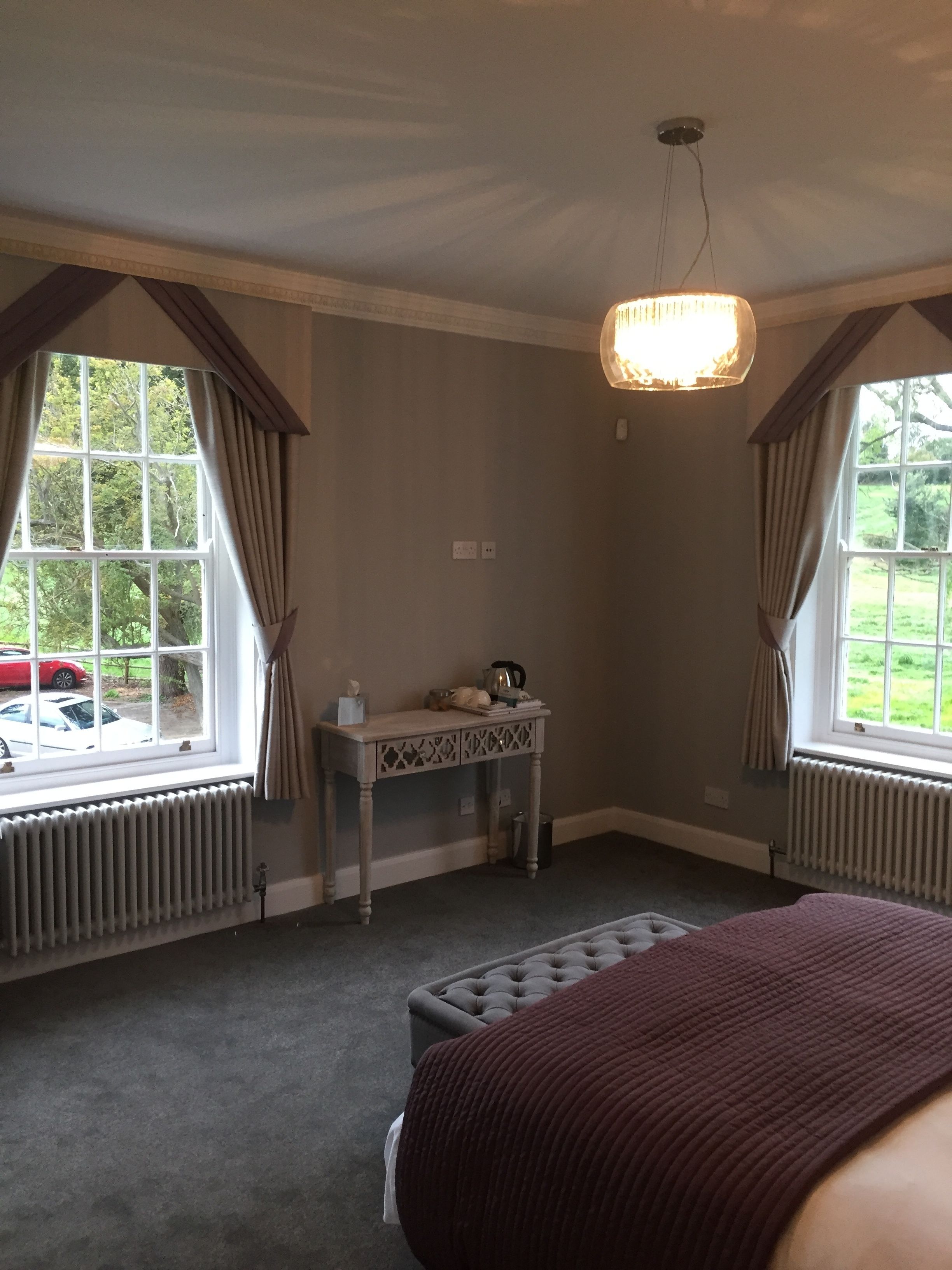 Un dormitorio con cama, mesita de noche, radiador y ventana con cortinas.