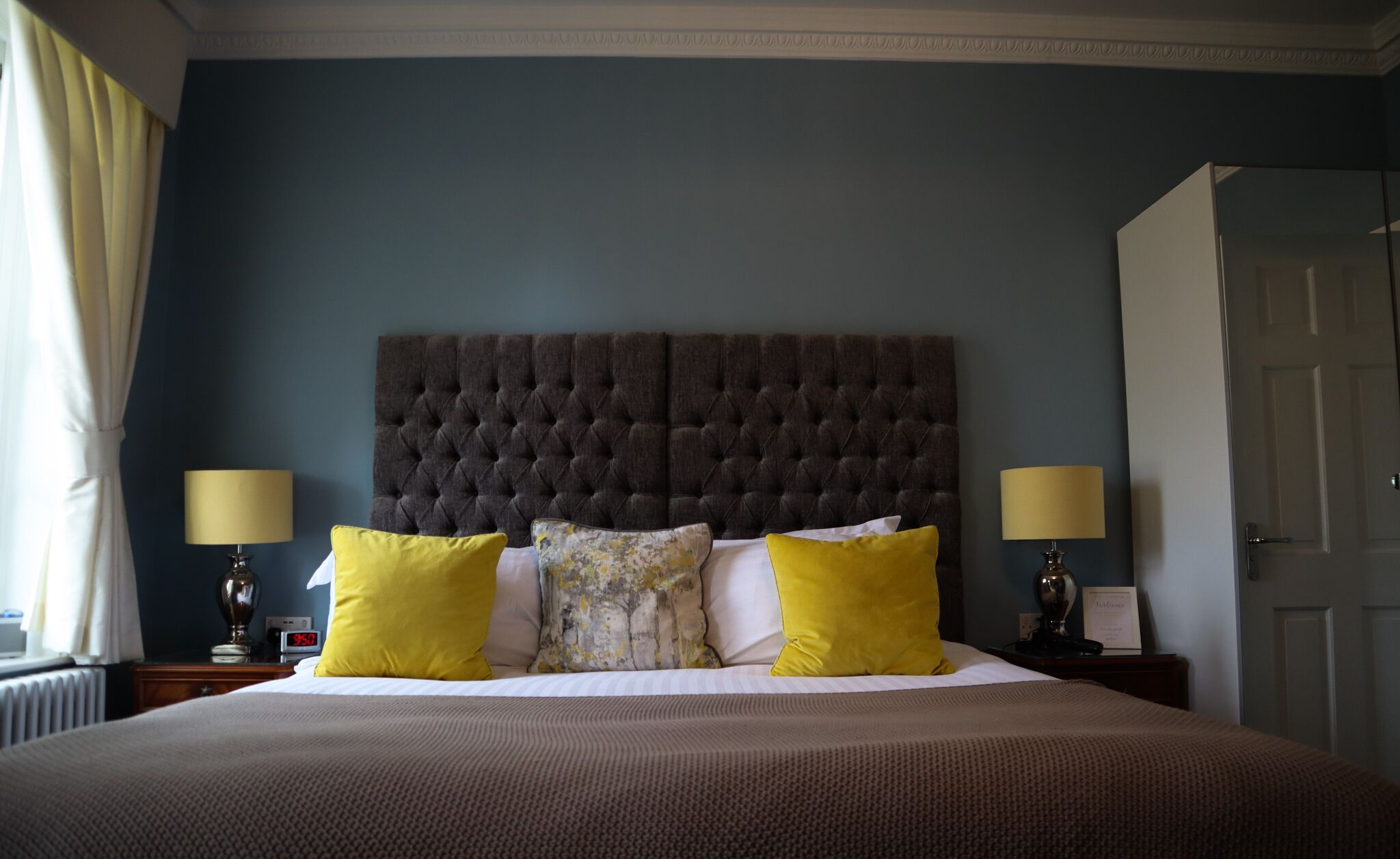 A neatly made bed with a tufted headboard, two bedside lamps, and a clock on the nightstand.
