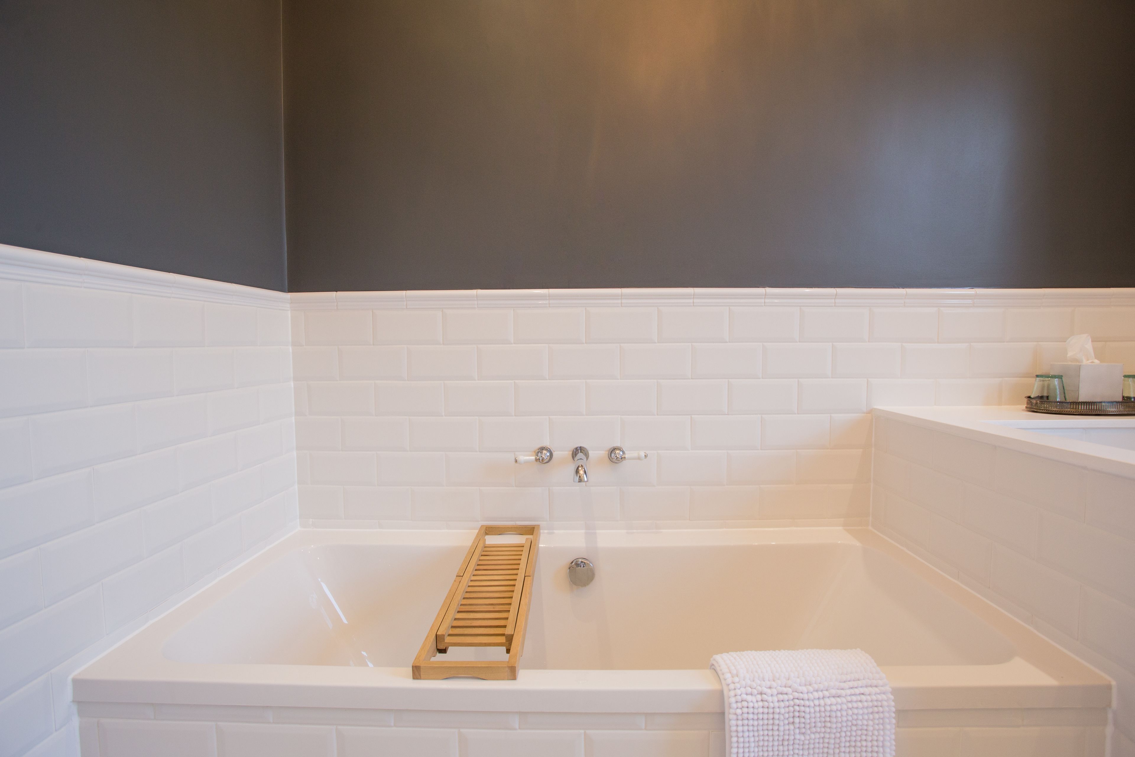 A modern bathroom with a white bathtub, a wooden tray, and a towel on the side.