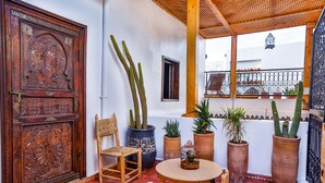 A courtyard with a wooden door, a woven chair, a round table, and several potted cacti. - Dar Dada Mouss (Marrakech)