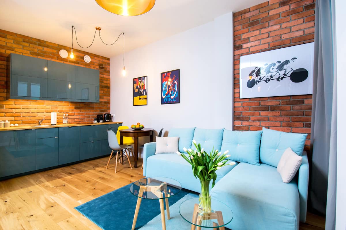 Een moderne woonkamer met een blauwe bank, een glazen salontafel en een vaas met bloemen.