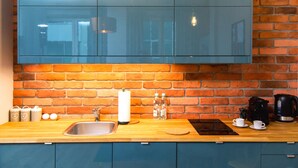 Una cocina con pared de ladrillo, encimera de madera, armarios azules, un lavamanos y una cafetera.