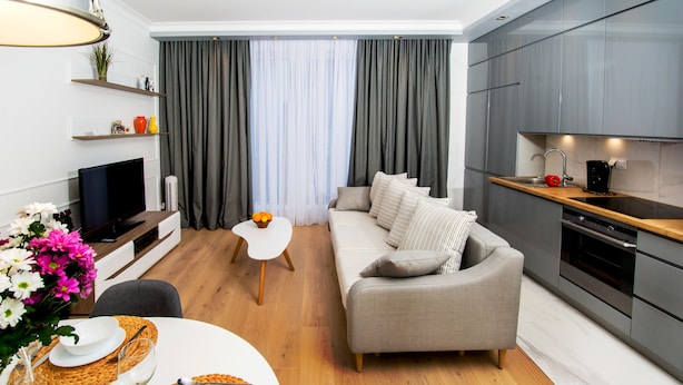 Una sala de estar moderna con sofá, una mesa de comedor con platos y vasos, televisor y una cocina con armarios y estufa.