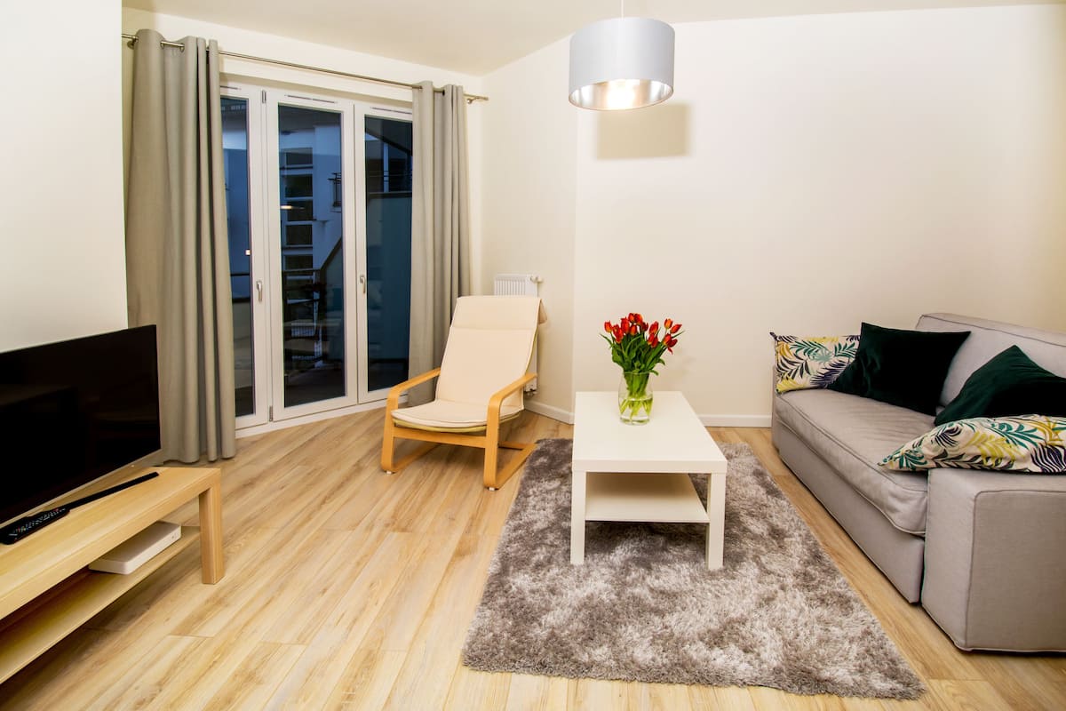 Een moderne woonkamer met een flatscreen televisie, een bank, een stoel, een salontafel en een vaas rode bloemen.
