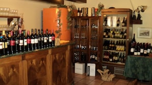 Een bar met een houten toonbank waarop verschillende flessen wijn staan. Achter de toonbank zijn er schappen met meer flessen en glazen.