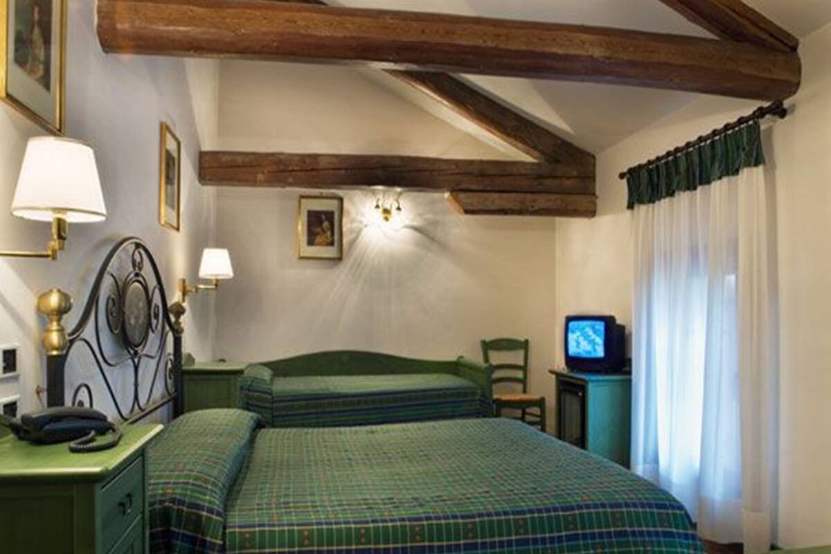 Una habitación con cama, escritorio, silla, televisión y ventana con cortinas.