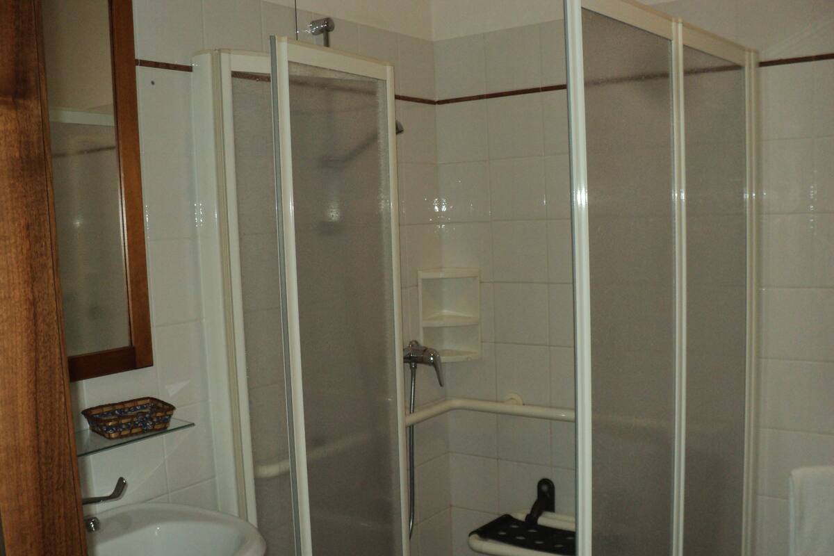 Un baño con ducha envuelta en vidrio, un lavabo blanco y un espejo sobre el lavabo.