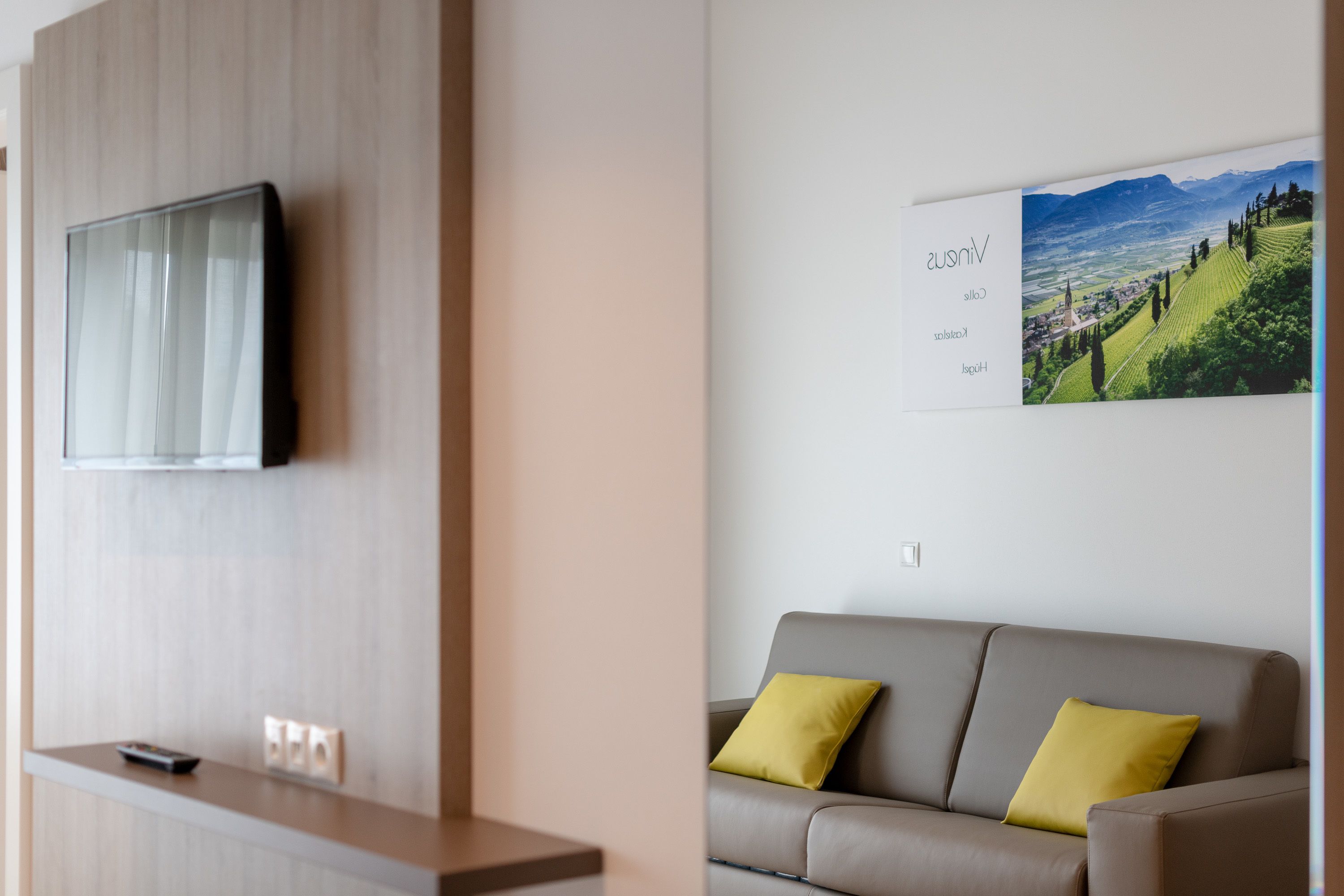 Una habitación de hotel moderna con un televisor de pantalla plana montado en la pared, un mostrador de recepción de madera y un sofá con cojines amarillos.