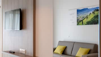 Une chambre d’hôtel moderne dotée d’un téléviseur à écran plat fixé au mur, d’un comptoir d’accueil en bois et d’un canapé avec des coussins jaunes.