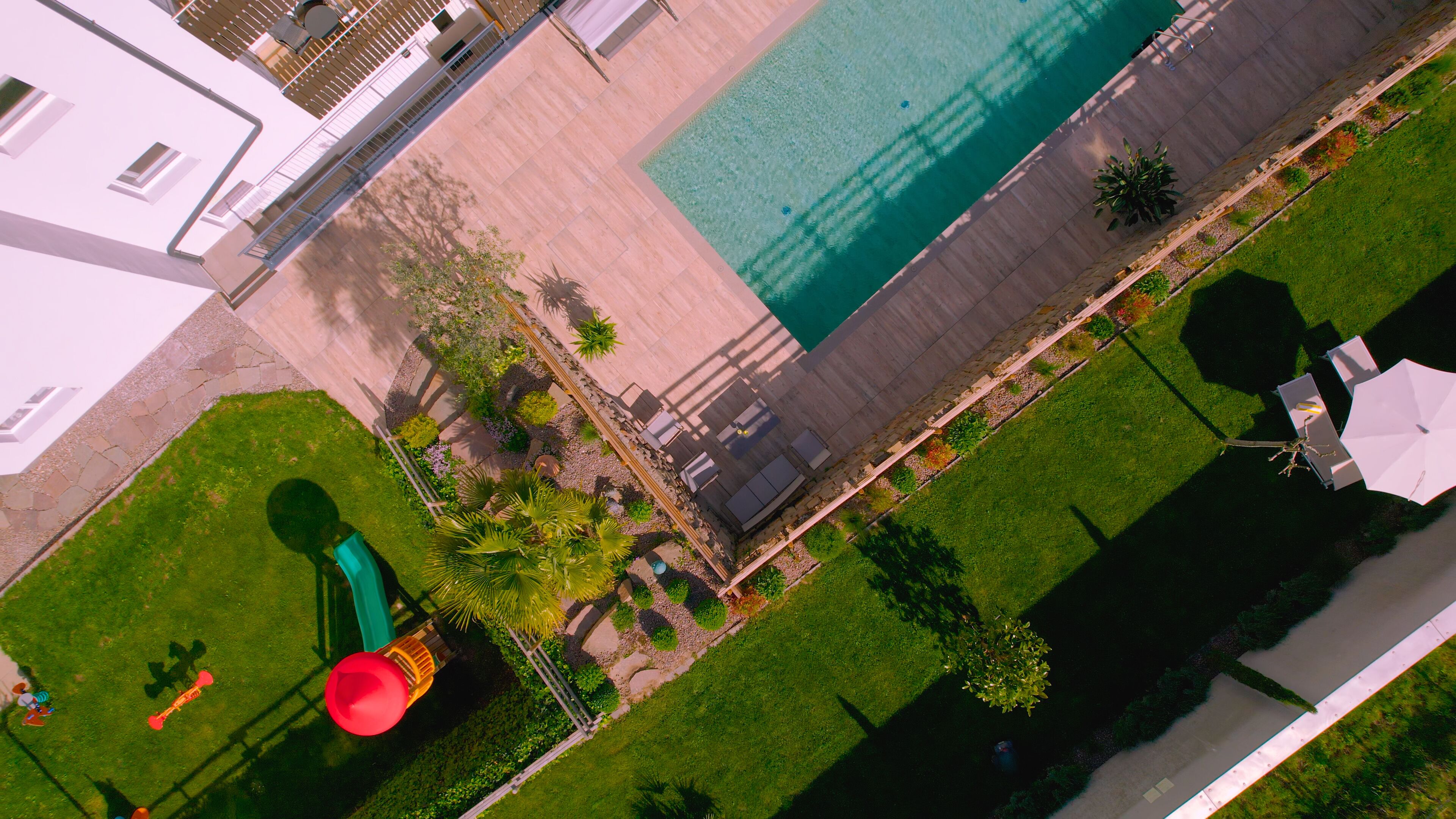 An aerial view of a residential area with a swimming pool, a children's play area, and a well-maintained lawn.