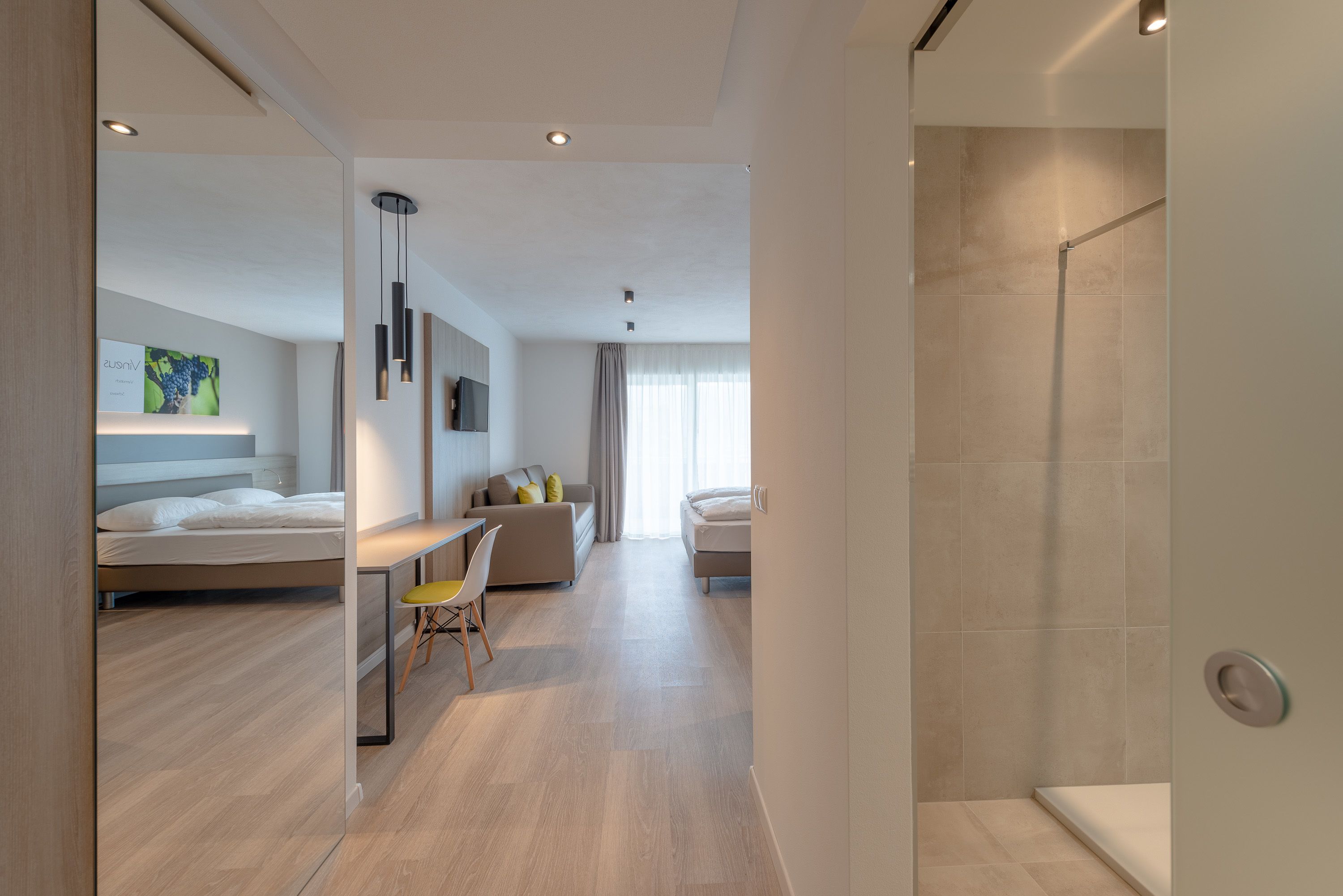 A modern hotel room with a bed, a desk, a chair, and a shower area.