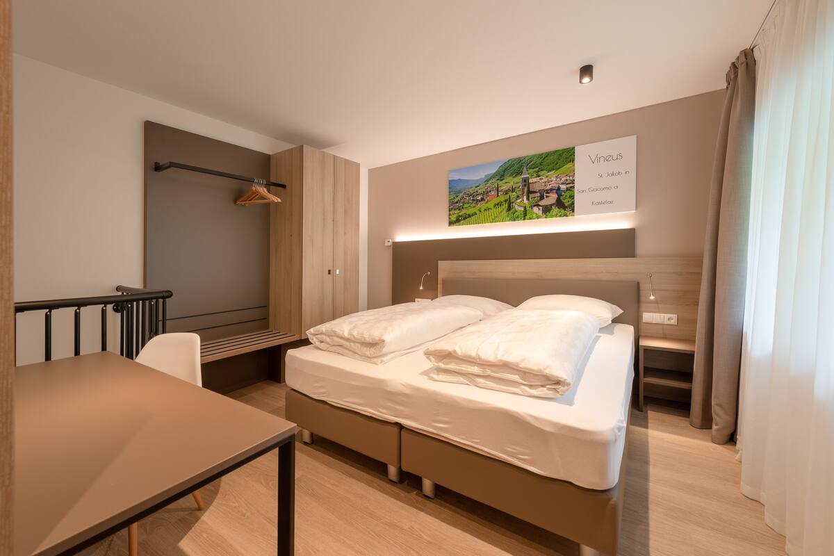 A modern hotel room with a bed, a desk, and a wall-mounted picture.