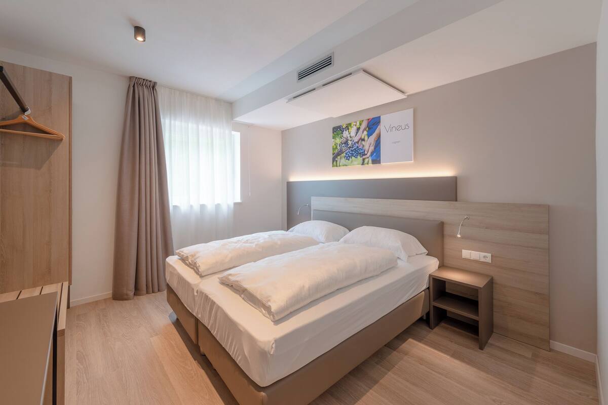 A modern bedroom with a bed, bedside tables, a hanging light, and a window with curtains.