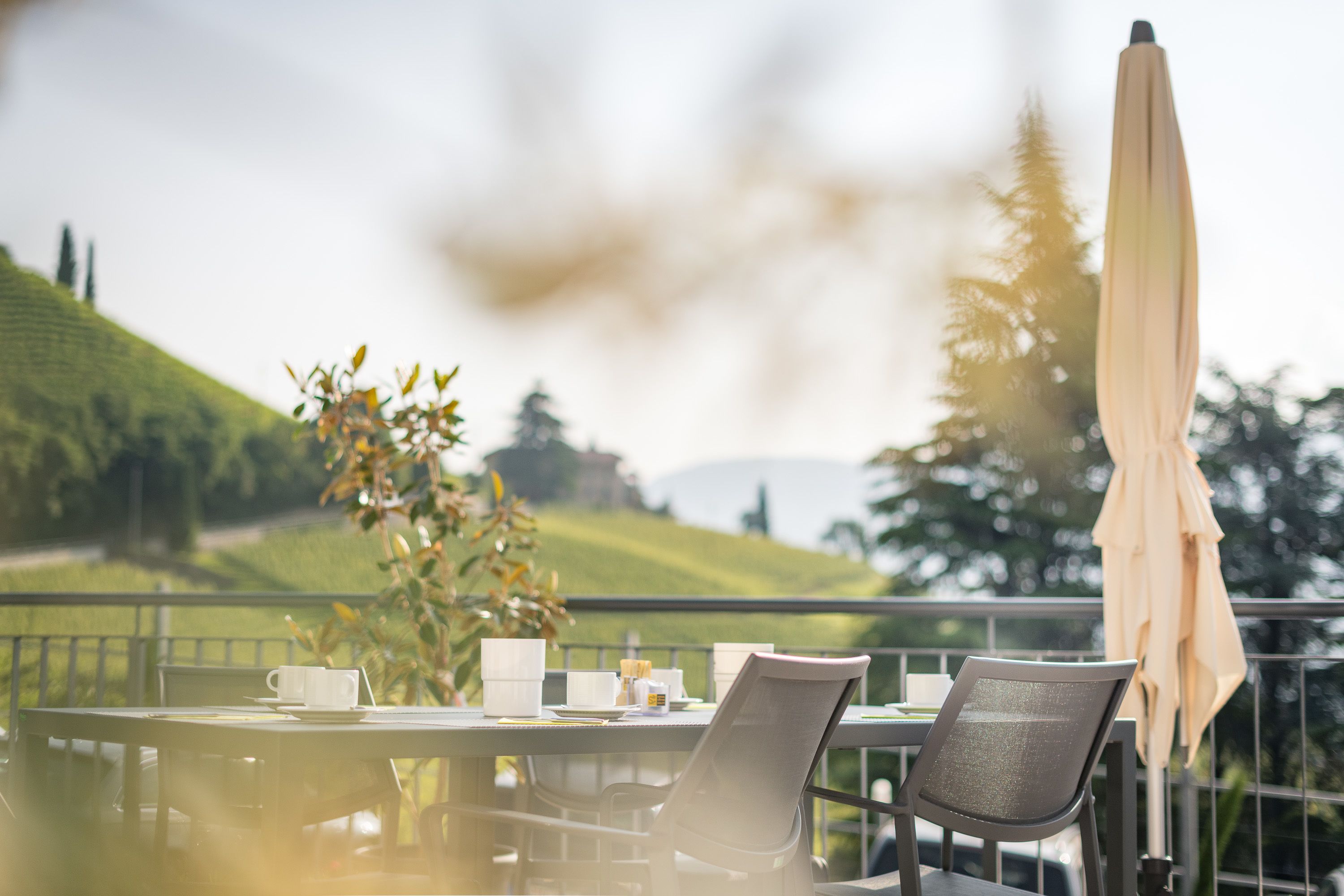 A table with chairs and a table umbrella on a balcony overlooking a green landscape.