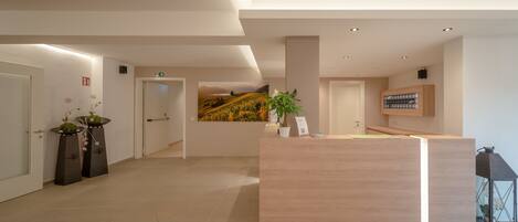 A modern reception area with a wooden reception desk, potted plants, and a wall-mounted TV.
