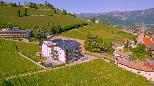 A modern building with solar panels, surrounded by vineyards and a church in the background. - Vineus (Termeno Sulla Strada del Vino)