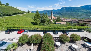 A parking area with several cars, a vineyard, and a church with a tall spire. - Vineus (Termeno Sulla Strada del Vino)