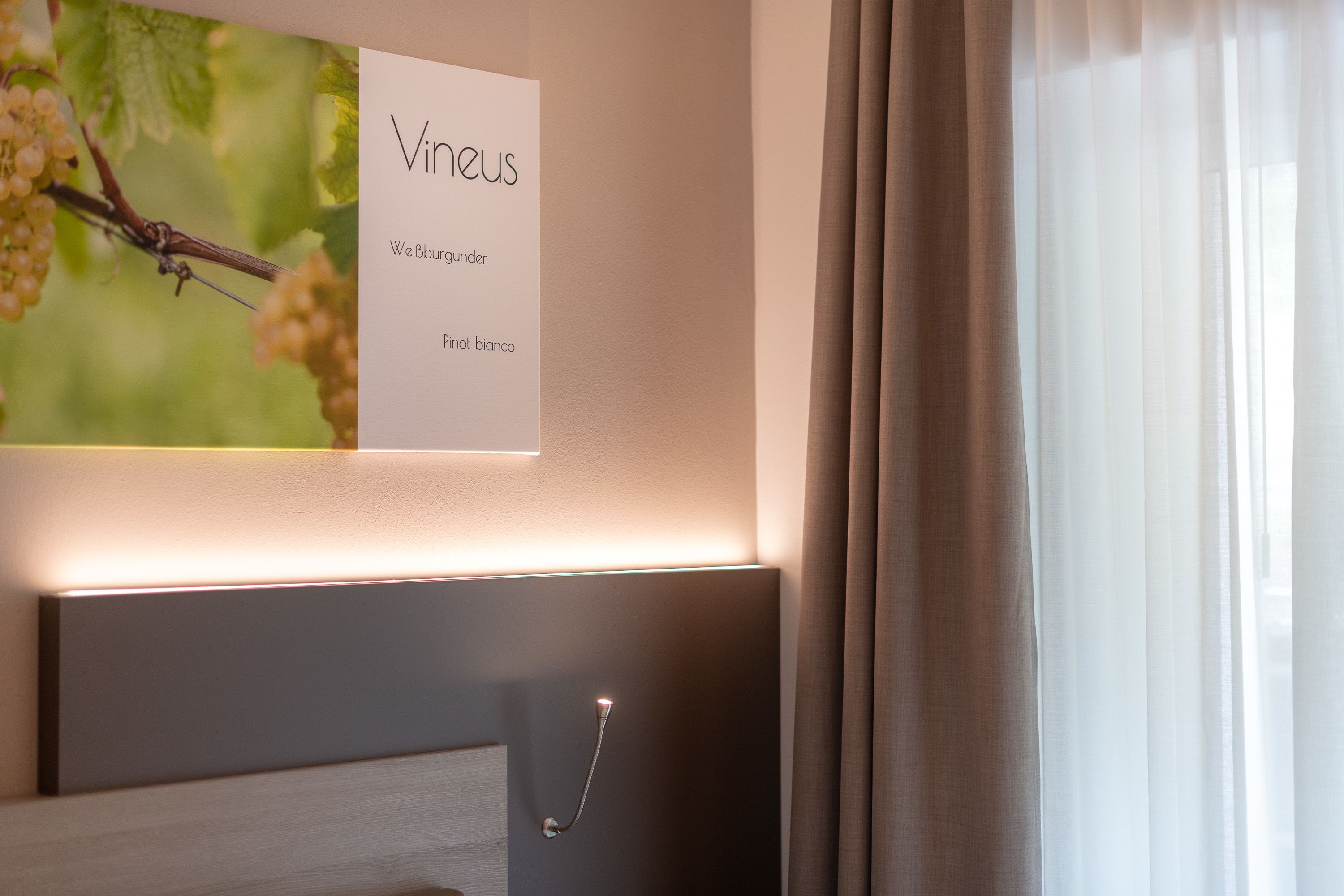 Une chambre d’hôtel avec un tableau représentant des raisins, une table de chevet et un luminaire fixé au mur.