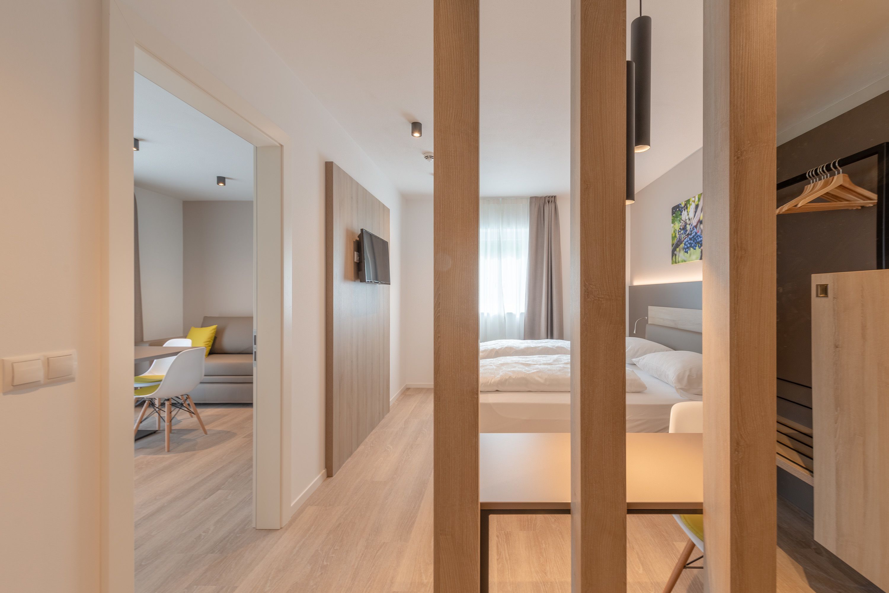 Una habitación de hotel moderna con piso de madera, una cama, un escritorio con silla, un televisor montado en la pared y un armario.