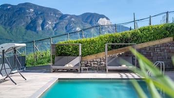 Zona de piscina con sillones de descanso y vistas a montañas.
