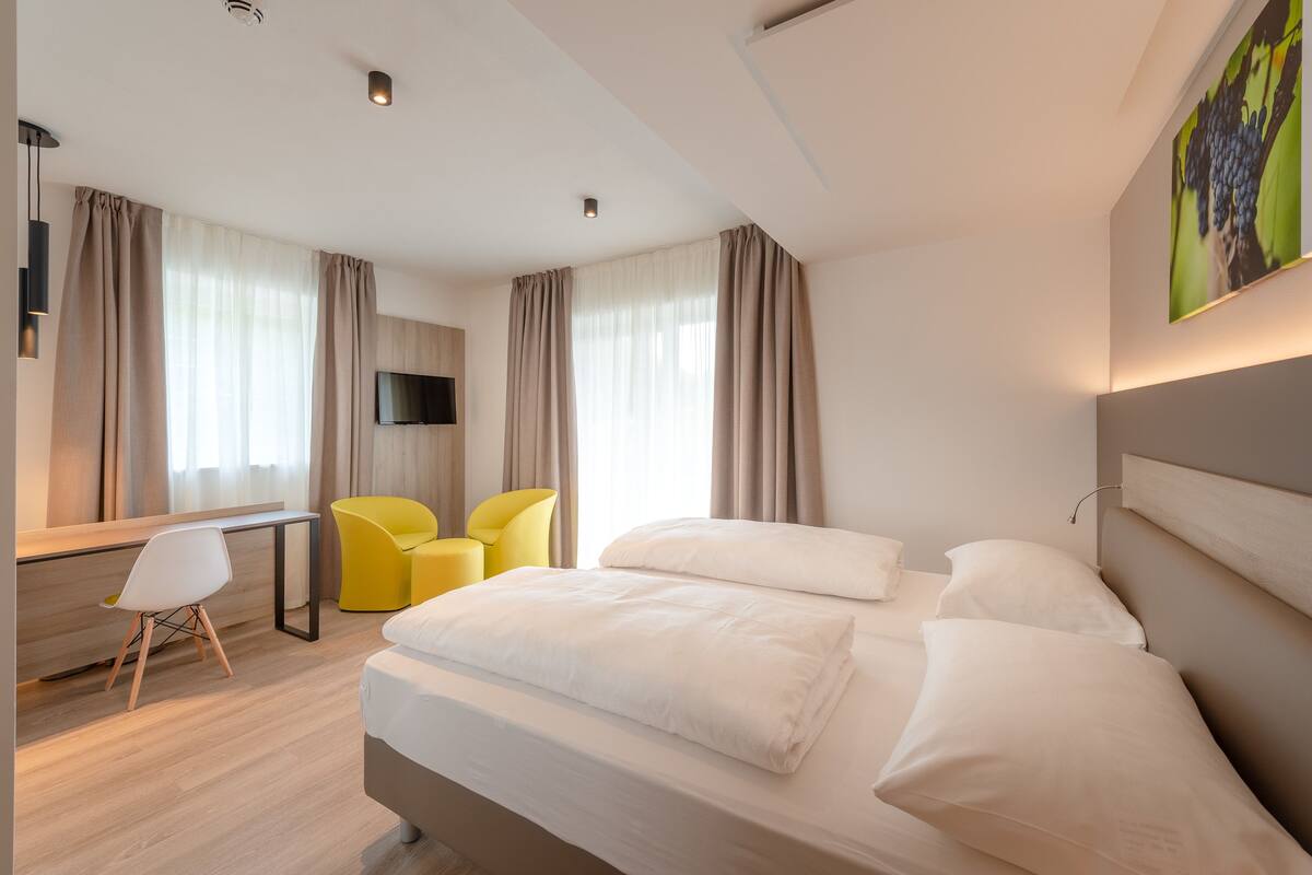A modern hotel room with a bed, a desk, a chair, and a TV.