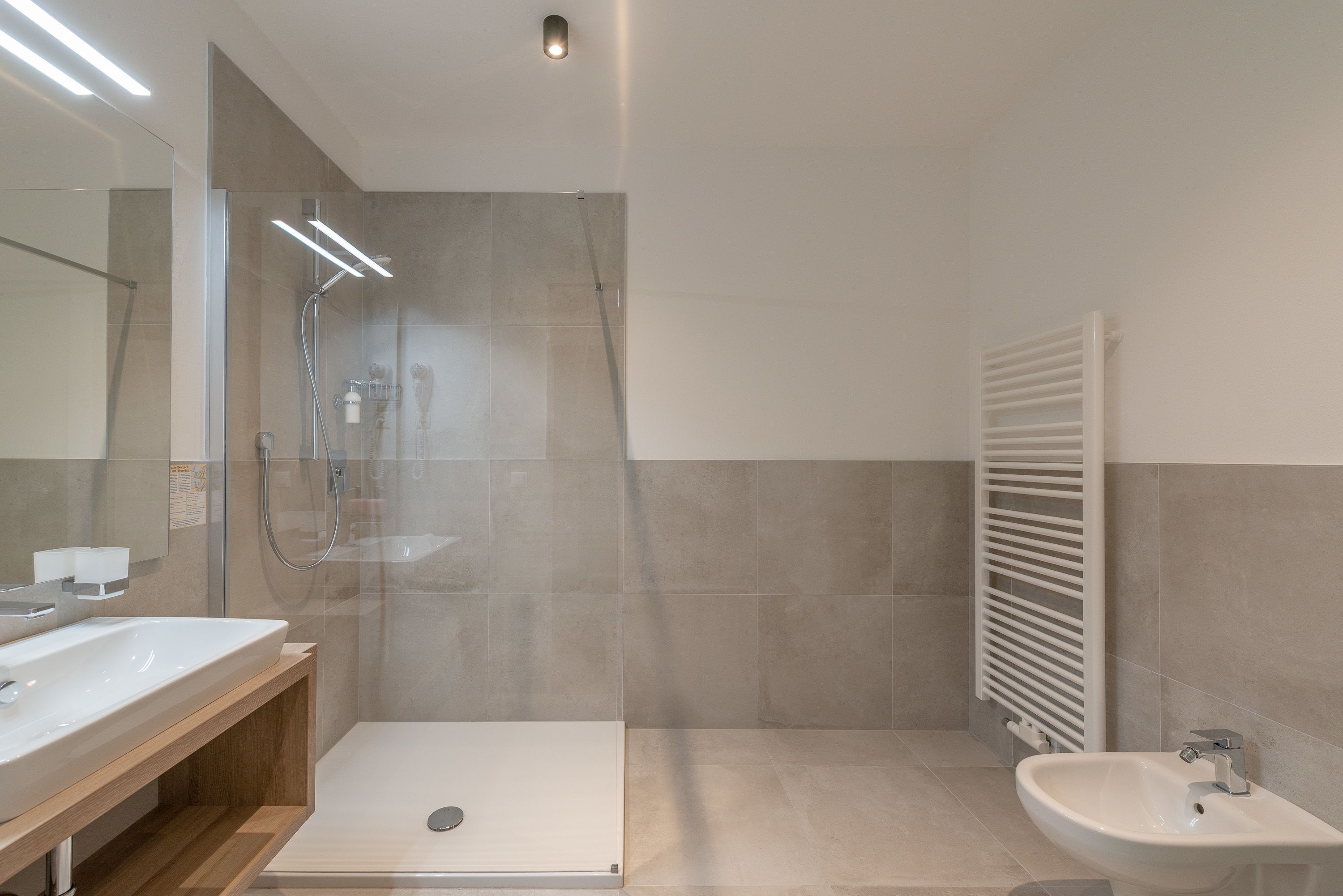 A modern bathroom with a glass-enclosed shower, a wooden vanity, and a white sink.