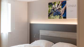 Ett hotellrum med en säng, en sänggavel och en tavla på väggen som föreställer druvor och en person.