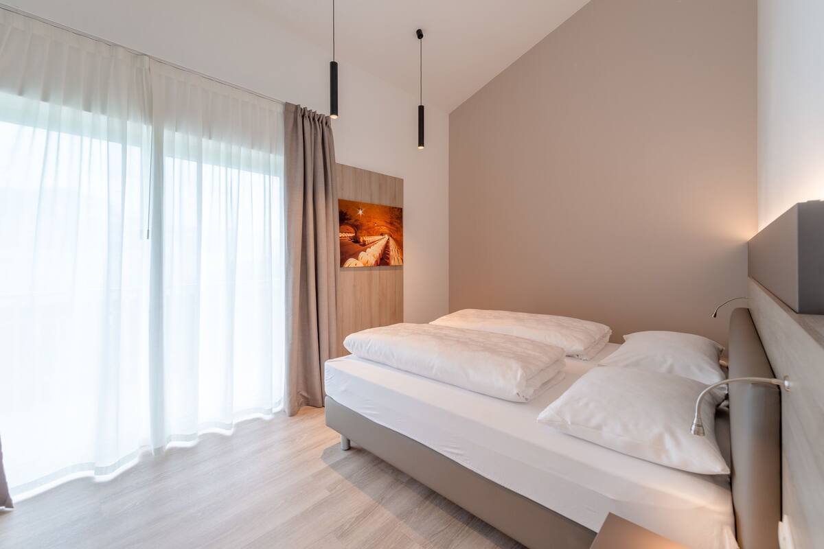 A modern bedroom with a large bed, a painting on the wall, and a window with sheer curtains.
