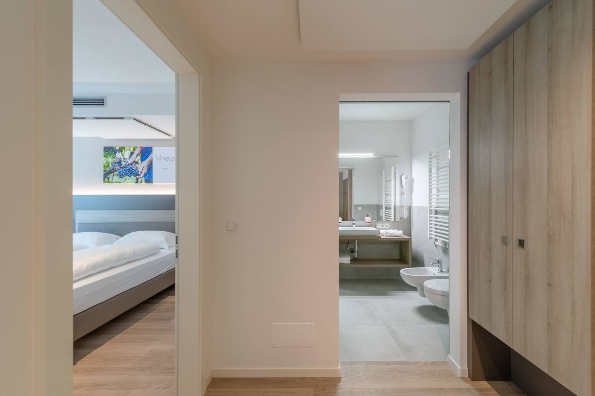 A modern bedroom with a bed, a bedside table, and a wall-mounted air vent.
