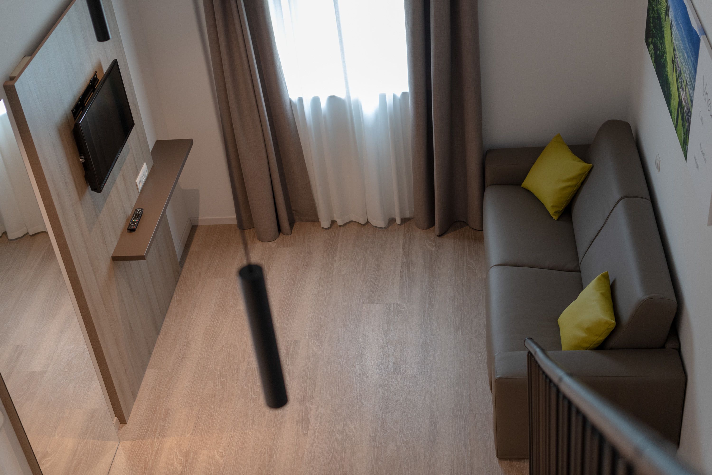Un salon moderne avec un téléviseur à écran plat fixé à un mur en bois, un canapé gris agrémenté de coussins jaunes et un plancher en bois.
