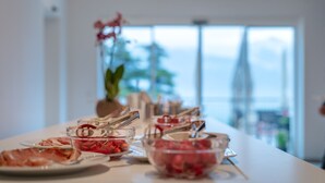 A buffet table with various food items and utensils, set against a bright interior with a large window in the background. - Vineus (Termeno Sulla Strada del Vino)