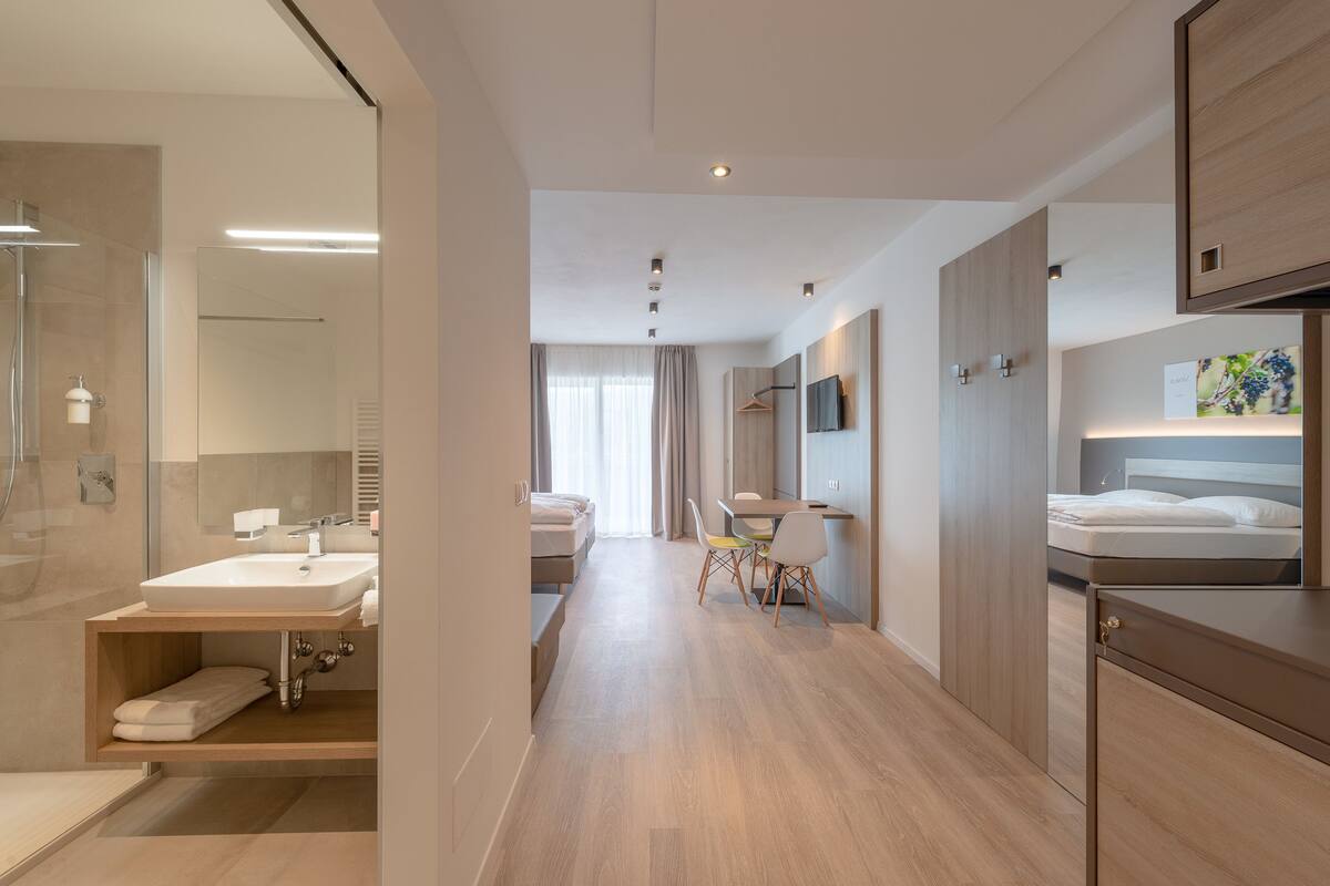 A modern hotel room with a bathroom, a dining area, and a bed.