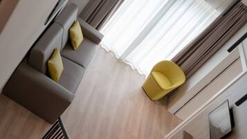 A modern living room with a grey sofa, yellow cushions, a yellow chair, and a large window with sheer curtains.