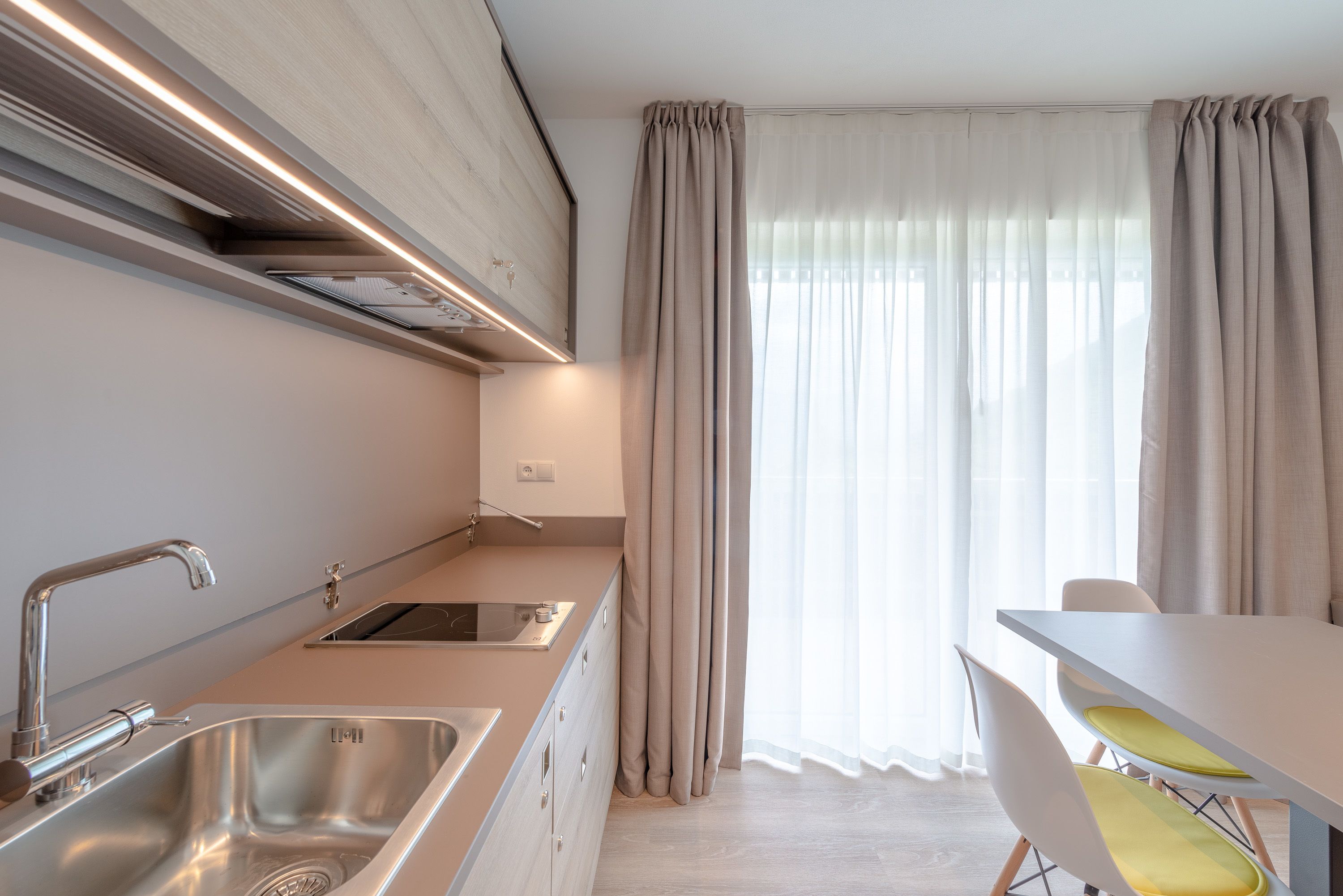 Una cocina moderna con electrodomésticos de acero inoxidable, un comedor con mesa y sillas, y un amplio ventanal con cortinas.