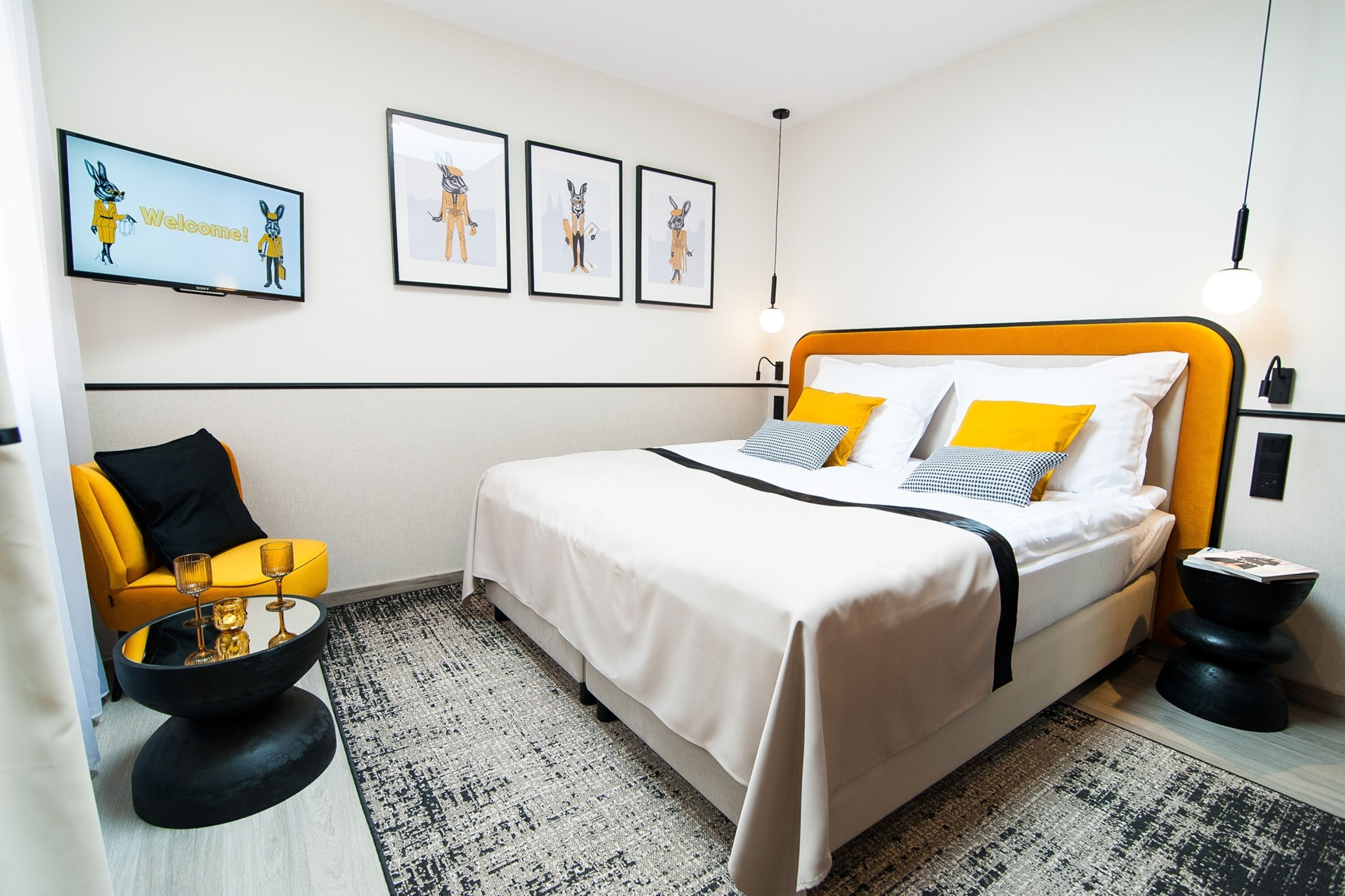 Un hotel moderno con una cama grande, un sillón amarillo, una mesa de centro negra y cuadros en la pared.