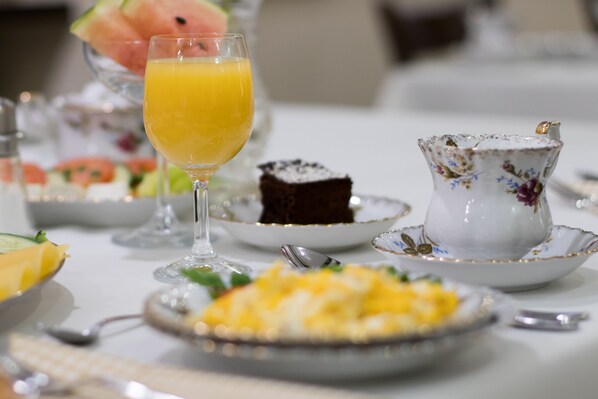 A breakfast setting with a glass of orange juice, a slice of watermelon, a plate of scrambled eggs, a piece of cake, and a floral teapot. - Hotel AWO (Gniezno)