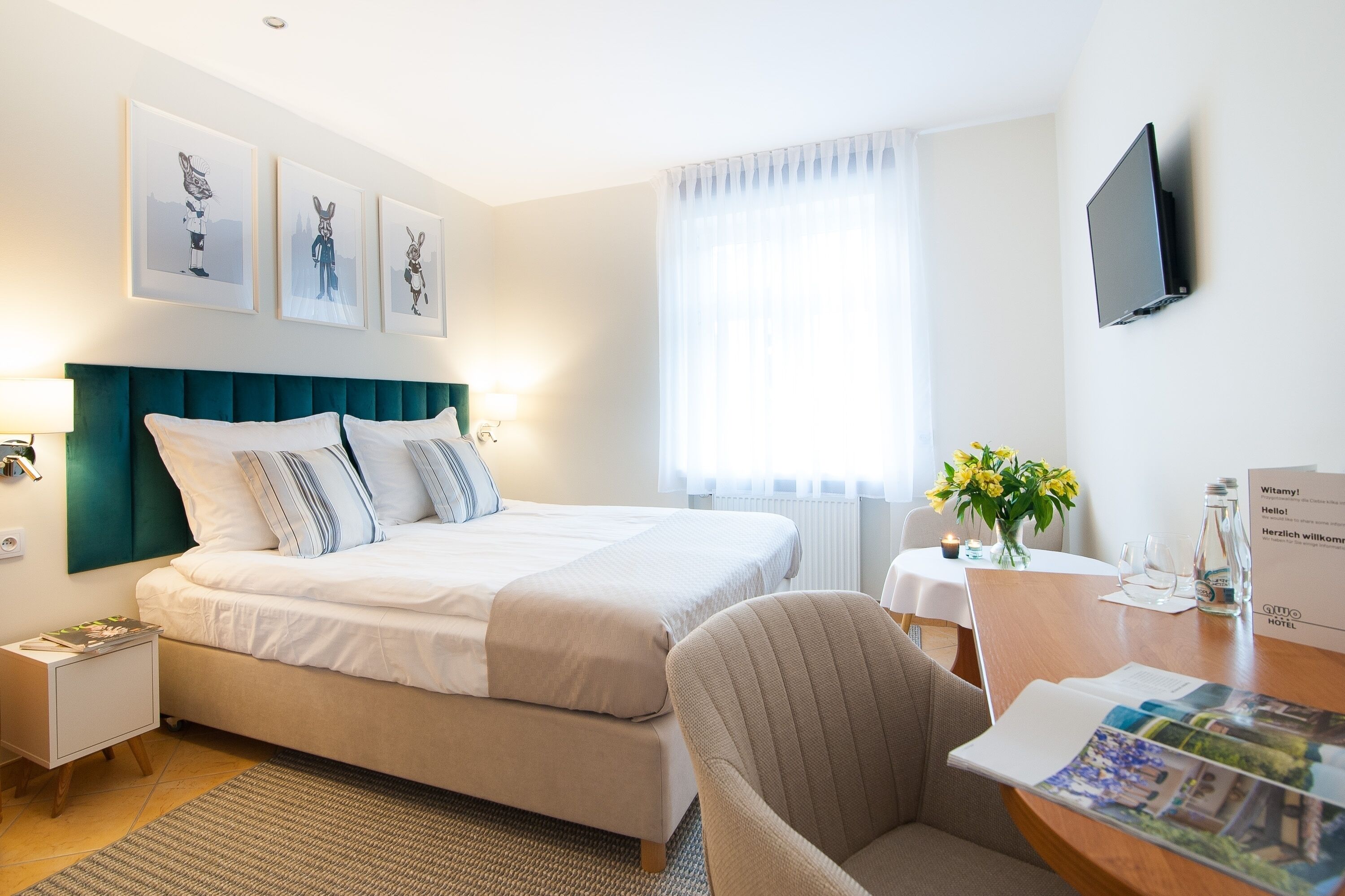 Habitación de hotel con cama, escritorio y silla, televisor en la pared y cuadros sobre la cama.