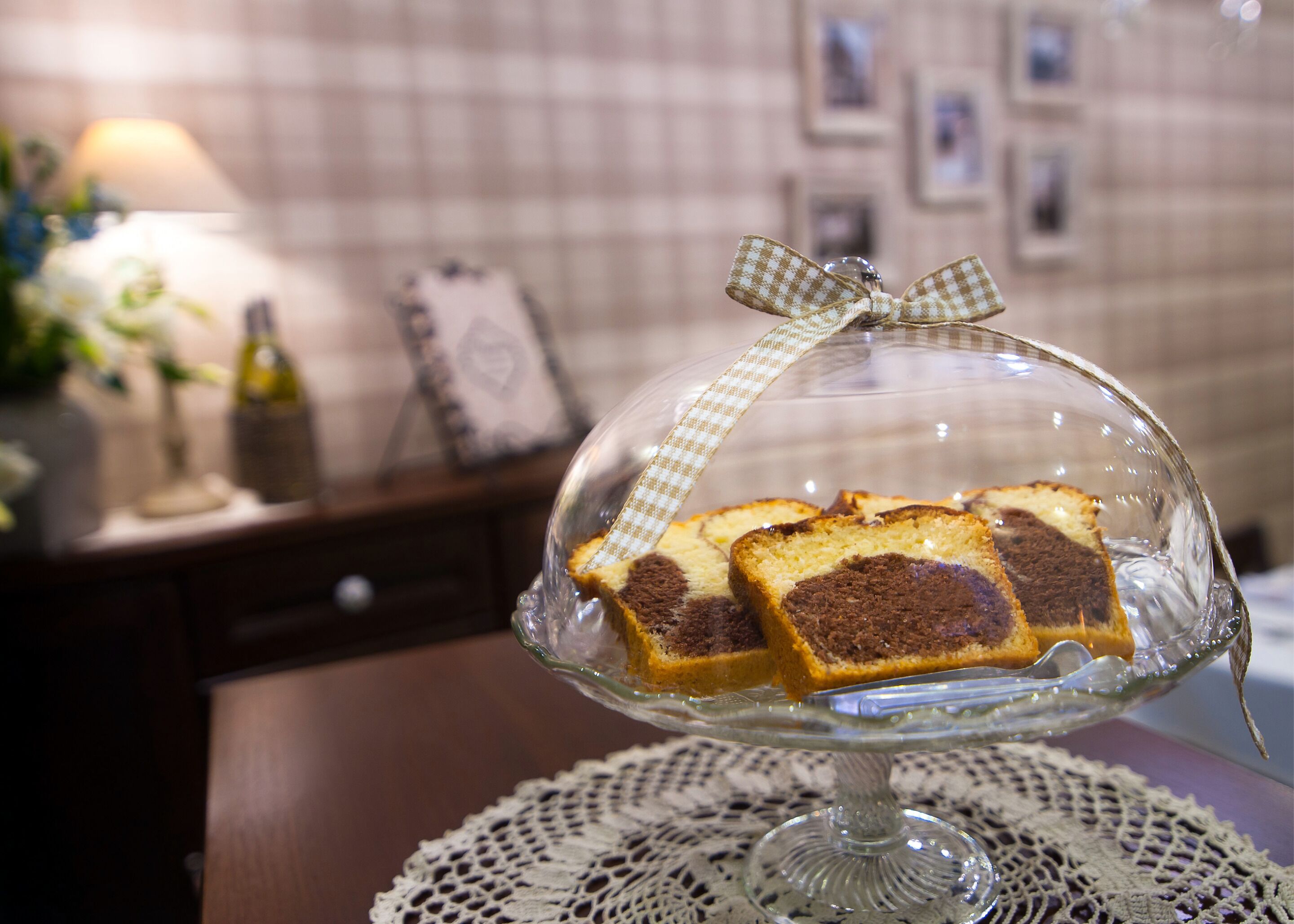 A glass dome cake stand with a checkered ribbon on a lace doily.