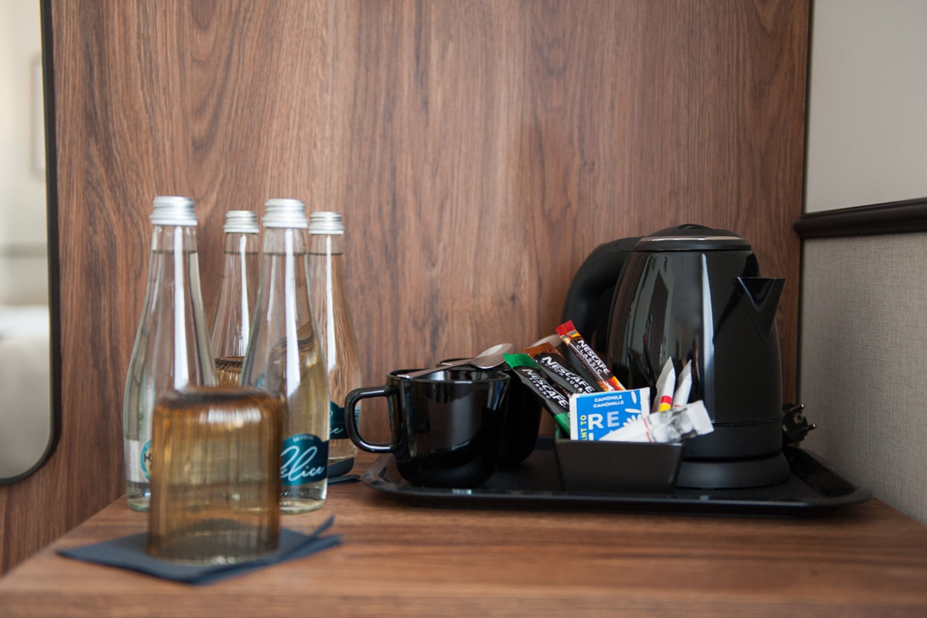A wooden table with a coffee maker, a tray with a black mug, and several glass bottles.