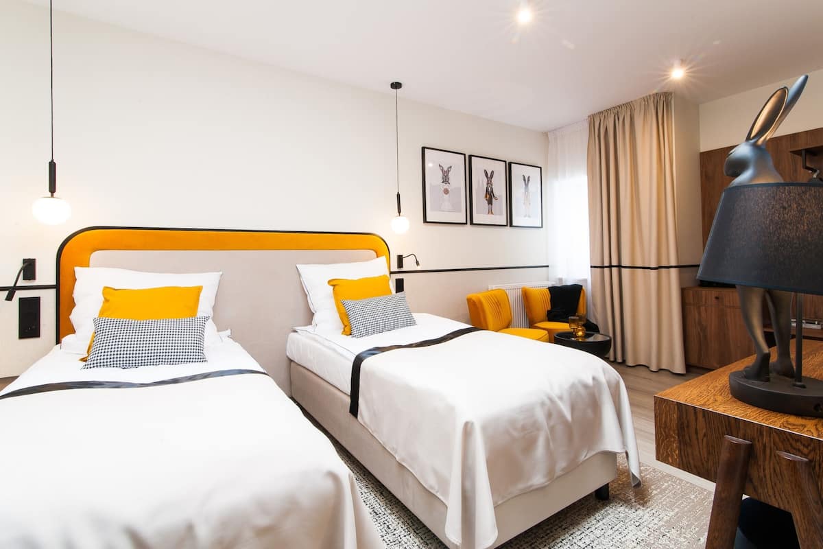 A hotel room with two beds, a desk, a lamp, and framed artwork on the wall.