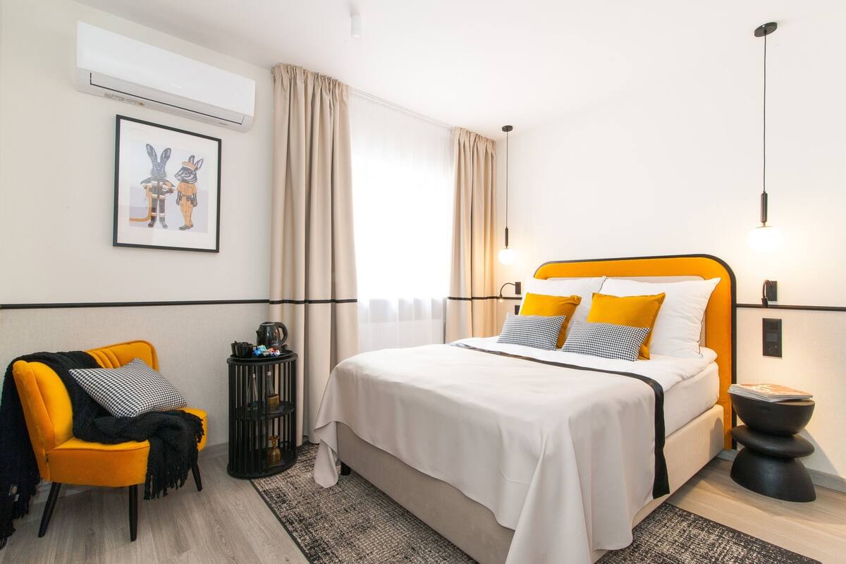 A modern hotel room with a bed, a chair, a small table, and a picture on the wall.